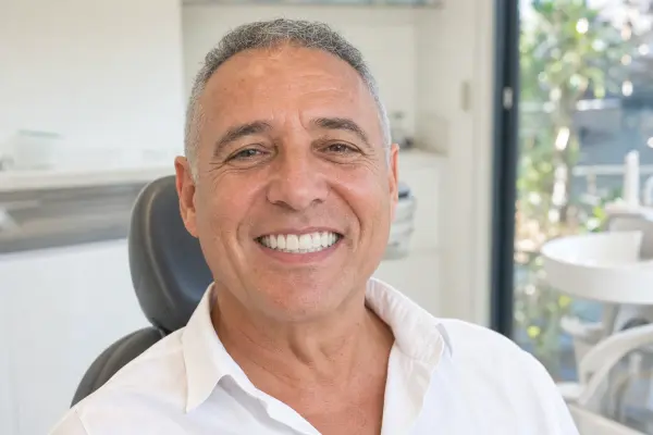מטופל יושב לאחר הטיפול וחושף חיוך מלא ואחיד של גשר קבוע על ארבעה שתלים, שמדגים שיקום שיניים של קשת מלאה.