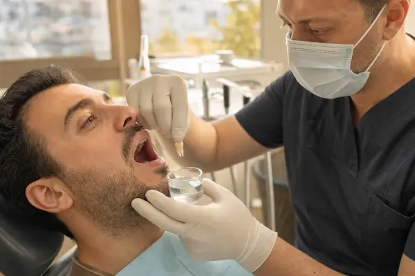 רופא שיניים עם כפפות מחזיק שן שניתקה ומליפה אותה מעל גביע סטרילי של סליין, מוכן להשתיל אותה בחלחולת המטופל בכיסא טיפולים מודרני.