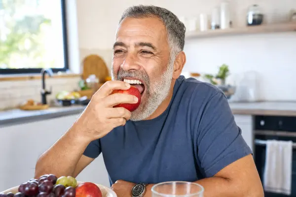 מטופל בבית אוכל תפוח וחיוך רחב המצביע על שחזור תפקוד וסטטיקה לאחר השתלת פה מלא.